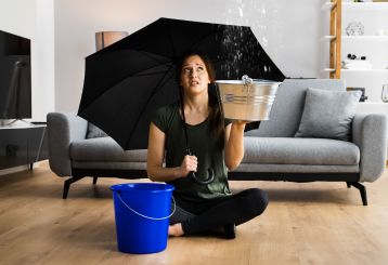 Woman holding an umbrella in a flooded home, emphasizing the need for professional flood damage restoration services.